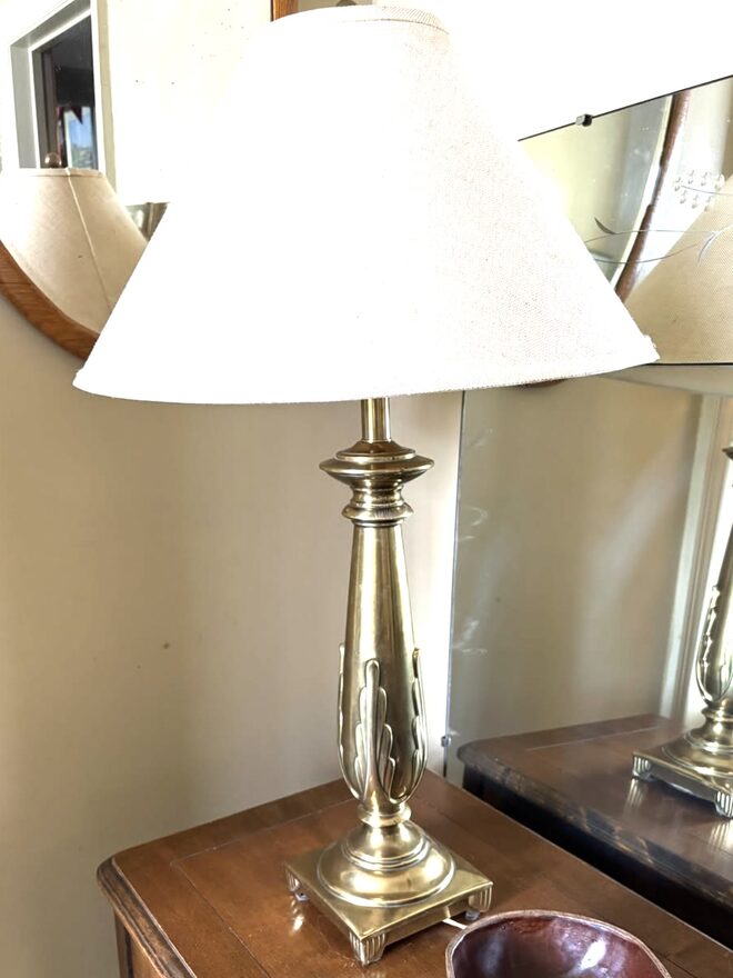 Brass table lamp with a tapering column wrapped in applied leaf ornament, on a square base with stepped feet, under an oatmeal linen coolie shade.