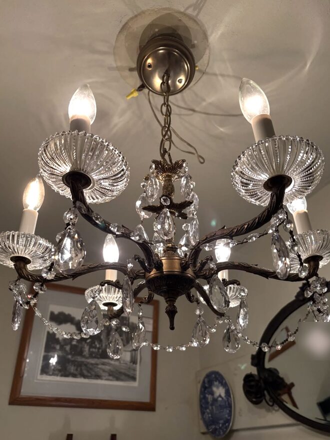 Six-arm chandelier with cast foliate brass arms, wide ribbed clear-glass bobeches under each candle light, pear-shaped crystal drops, and bead swags looping between the arms.