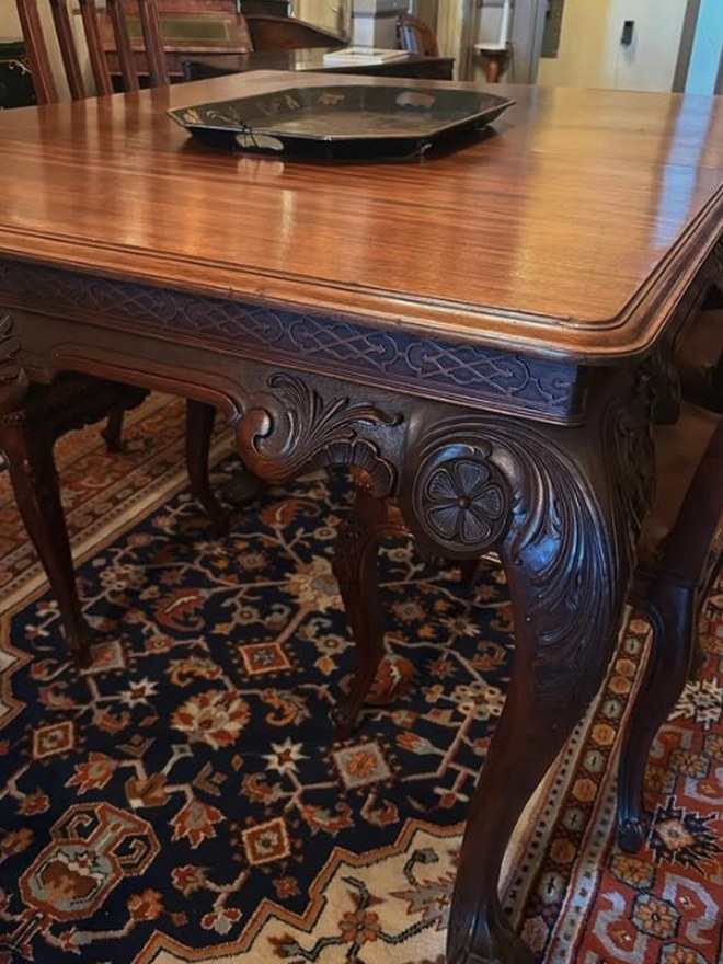 Hand-carved dining table with an acanthus-carved apron, cabriole legs, and ball-and-claw feet, standing on a Persian rug.