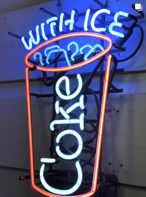 Vintage Coca-Cola advertising neon sign reading ‘Coke with Ice’ in blue and red tubing.