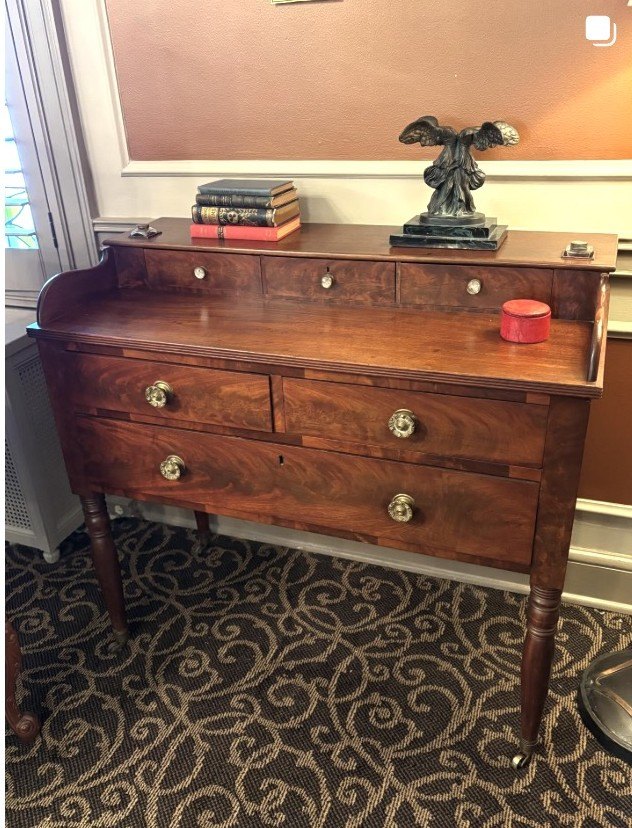 Empire mahogany sideboard topped with a carved bronze eagle and a stack of antique books.