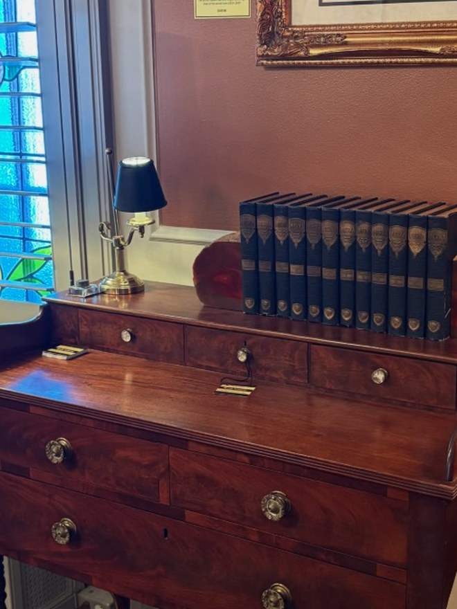 American Empire mahogany chest of drawers with a gallery back and original pressed-glass pulls, set below a stained-glass window.