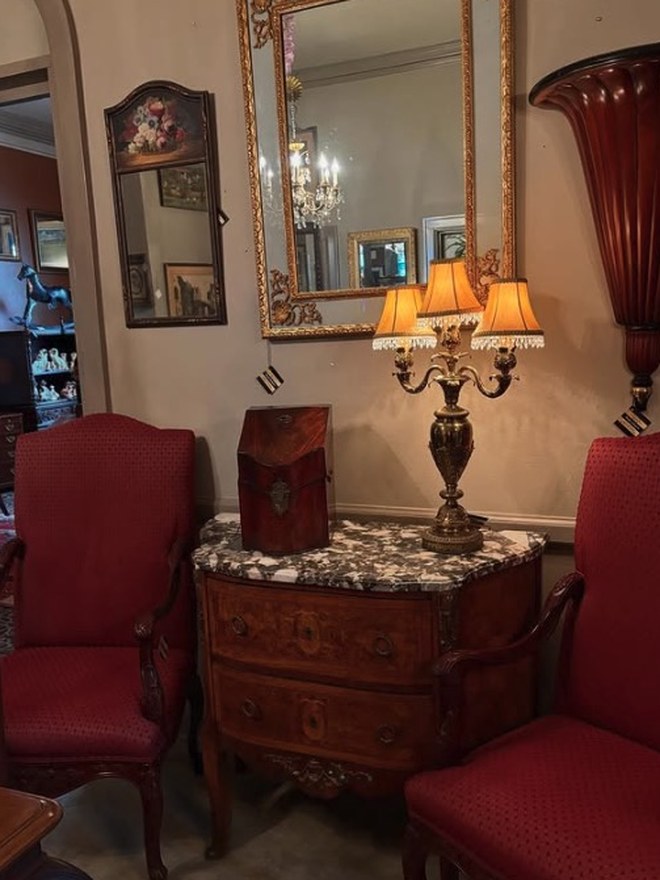French bombé commode with floral marquetry and a veined marble top, under a gilt mirror, flanked by two red upholstered armchairs.