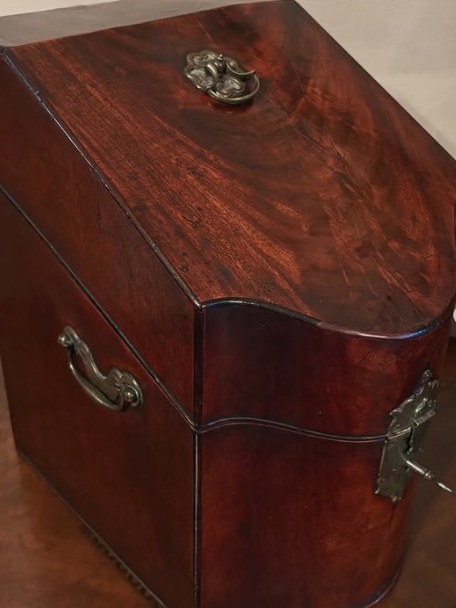 Georgian mahogany knife chest with a serpentine front, brass carry handle, and a scrolled brass escutcheon, key in the lock.