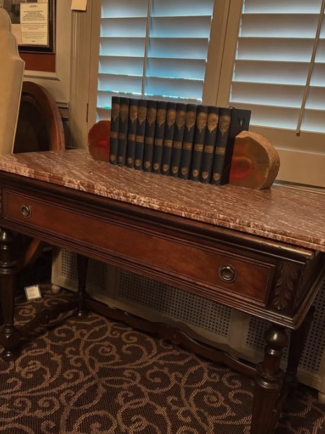 Victorian walnut library table with a rouge-marble top, a single carved drawer, and turned legs, holding a set of leather-bound books.