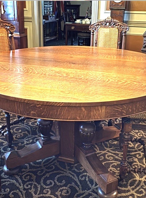 Round quartersawn tiger-oak pedestal dining table with a heavy carved base.