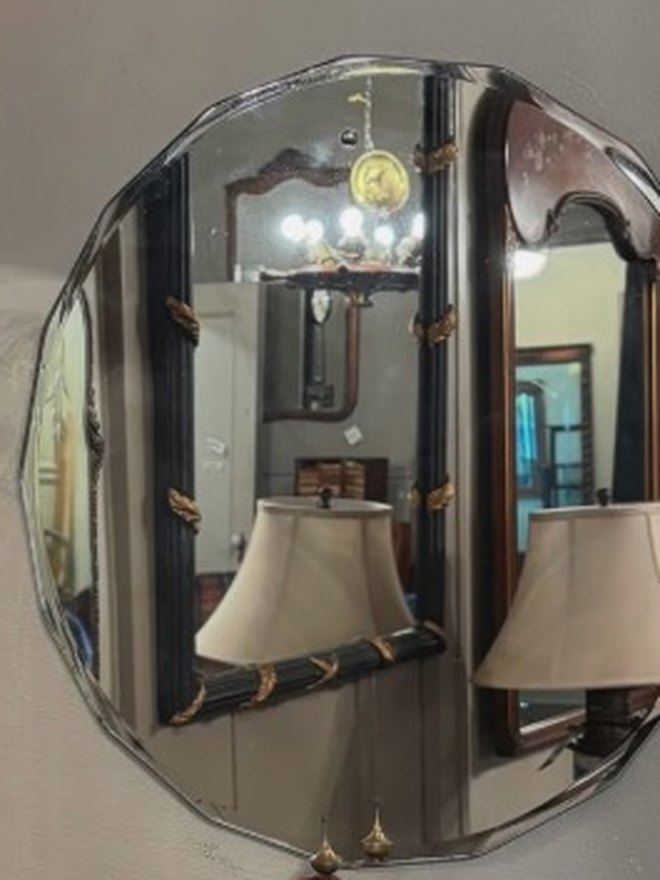 Round wall mirror with a scalloped, wavy bevel cut into the edge of the glass itself, hung above an oak sideboard.