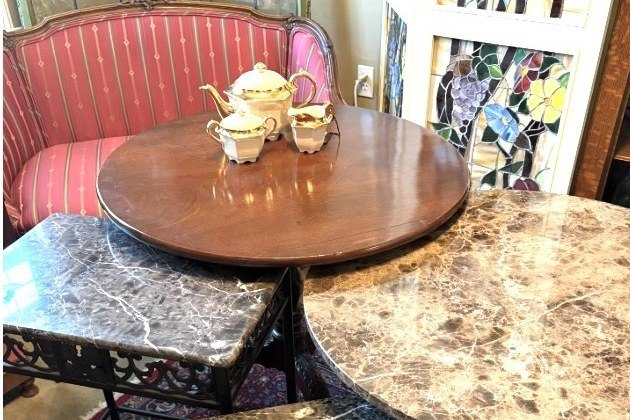 A corner of the booth: a striped settee and a gold tea set on a round table, with marble-top side tables in front of a stained-glass panel.
